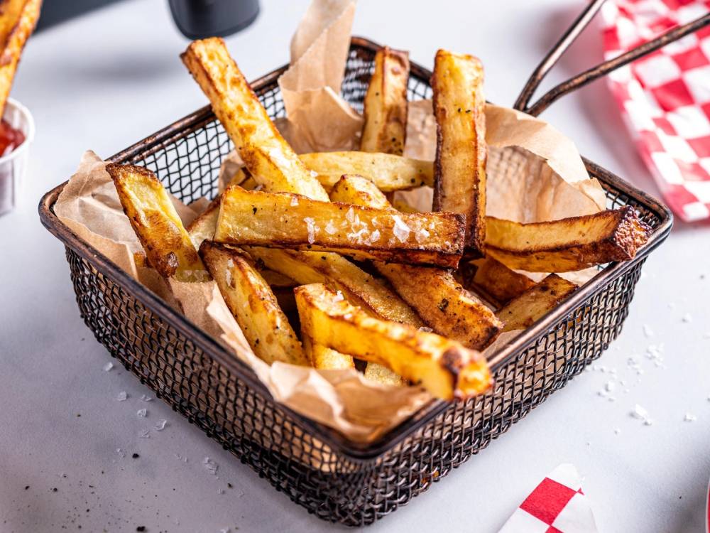 Sprøstekte pommes frites i en liten metallkurv med papir, klar til servering.