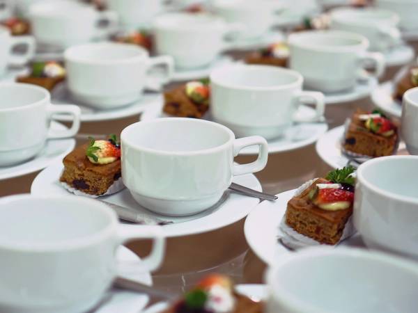 Kopper med kaffe og små stykker sjokolade med jordbær på fat, satt opp på et bord for selskap.