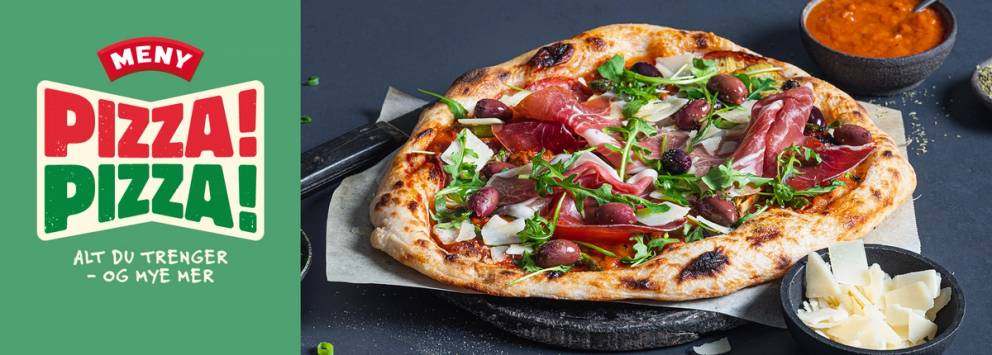 En pizza med skinke, ruccola og tomater på en svart stekeplate, med en liten bolle med saus og en skål med hvitløkssmør ved siden av.