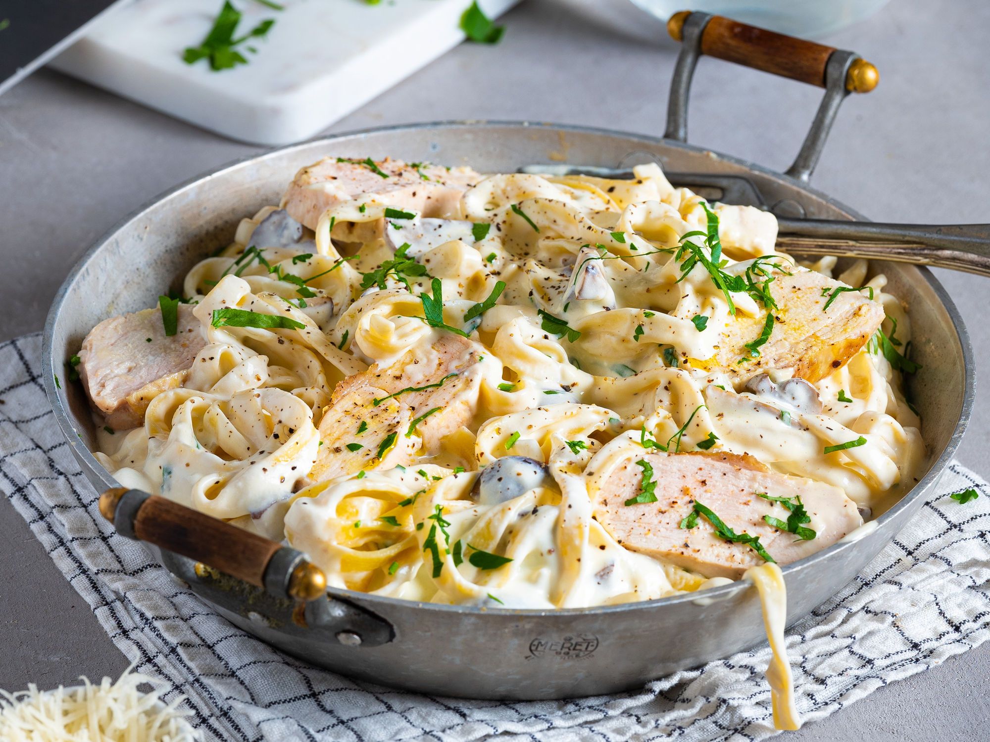Kremet pasta med kylling, sopp og frisk persille i en stor gryte på et kjøkkenbord.