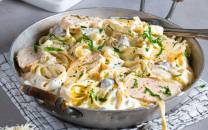 Kremet pasta med kylling, sopp og frisk persille i en stor gryte på et kjøkkenbord.