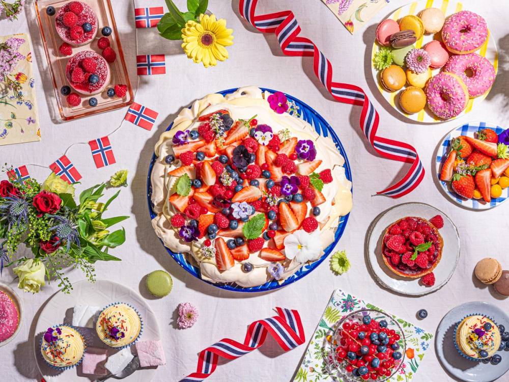Et bord med ulike kaker og småkaker pyntet med norske flagg og blomster, egnet for en sommerfeiring.
