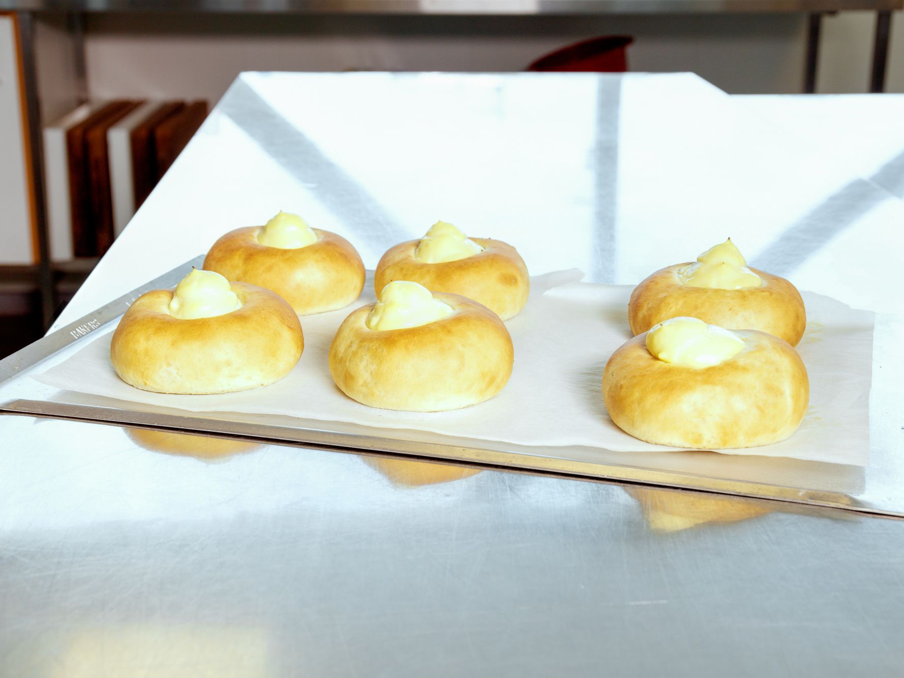 Fem små kaker med en klatt med hvit krem på toppen ligger på et hvitt serveringsfat.