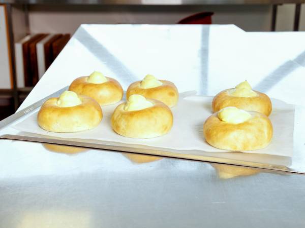 Fem små kaker med en klatt med hvit krem på toppen ligger på et hvitt serveringsfat.