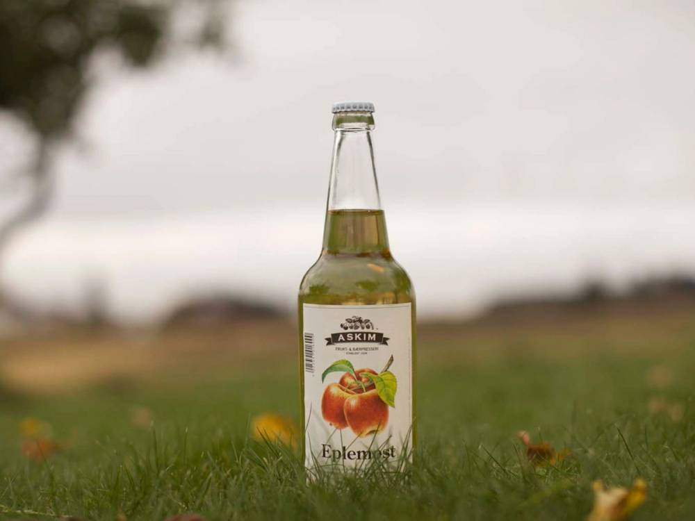 En glassflaske med eple- og bærjuice står på gress med en uskarp bakgrunn av natur.