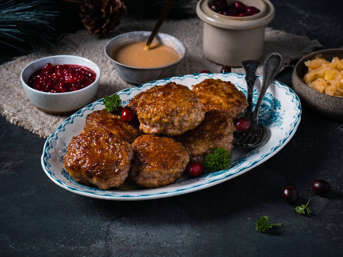 Stekte medisterkaker servert på et blått og hvitt fat med tyttebær og tilbehør i små skåler rundt omkring.