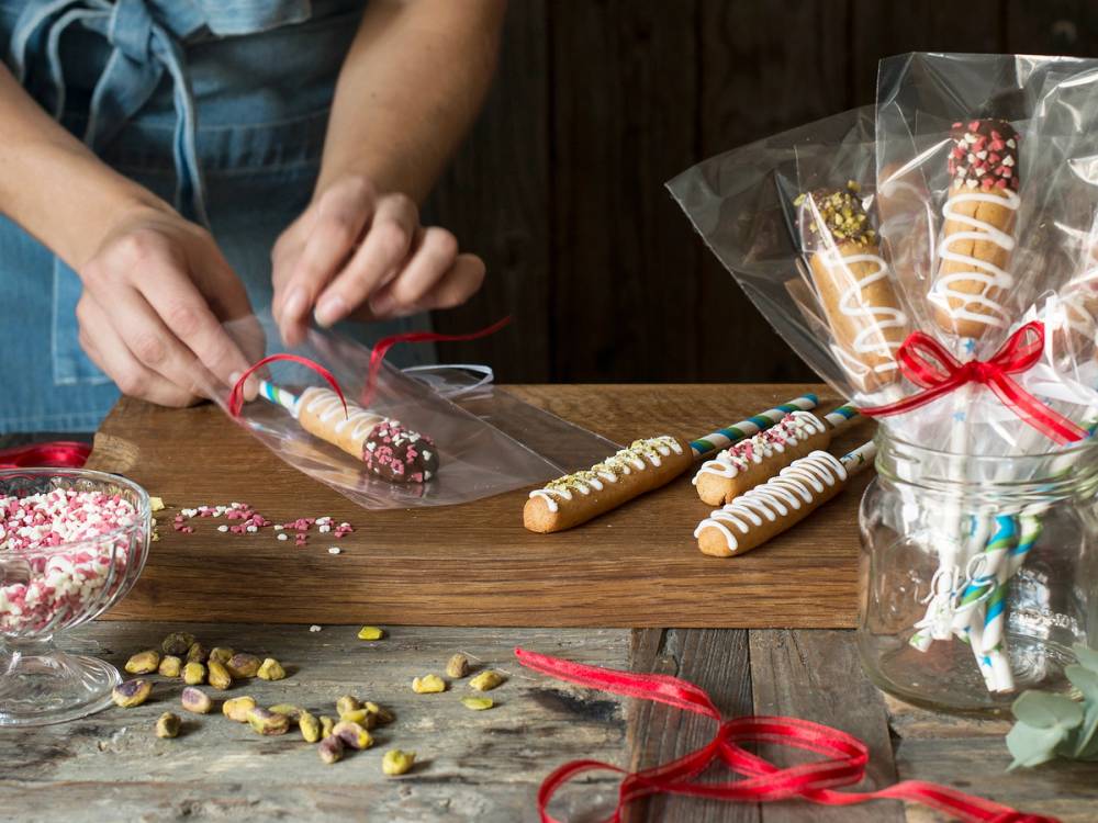 Person som pynter en kransekakestang med fargerike godteri og dekorasjoner på et bord.