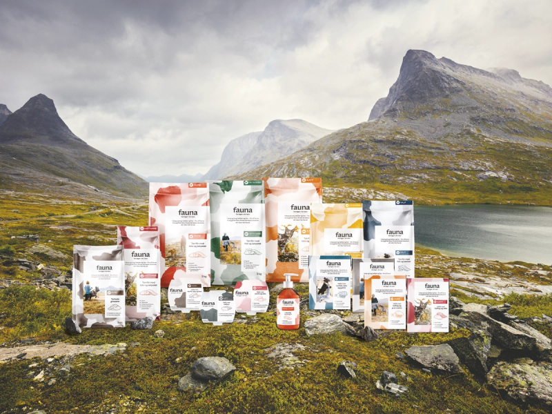 Pakker med dyrefôr eller kosttilskudd foran en fjell- og innsjølandskap, sannsynligvis i Norge.