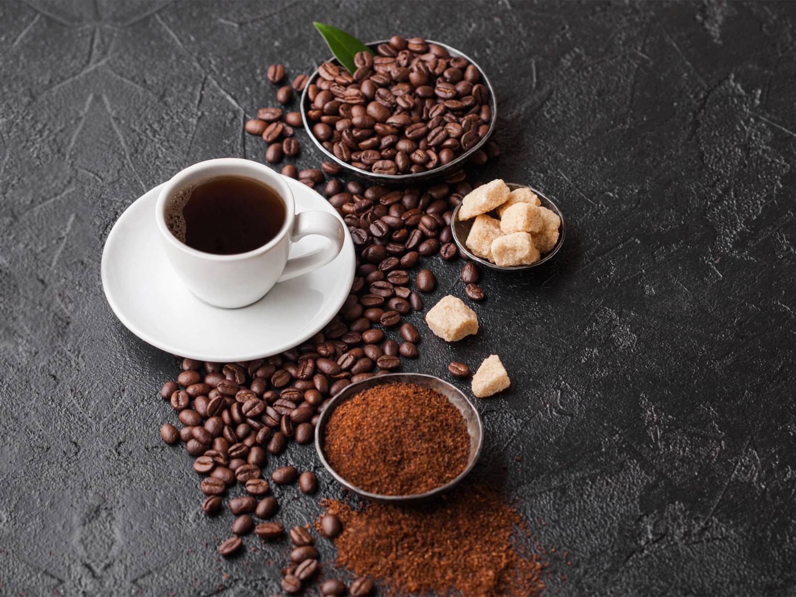 Kaffe med kaffebønner, sukkerbiter og malt på en mørk overflate