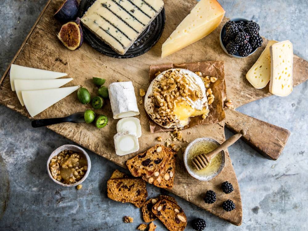 Et utvalg av oster, kjeks, druer og honning på et serveringsbrett.