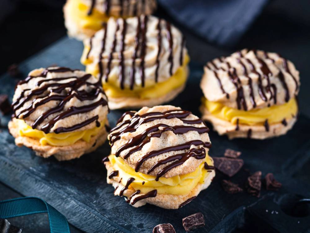 Ferske små kaker med gul krem og sjokoladestriper på toppen, plassert på en svart steinplate.
