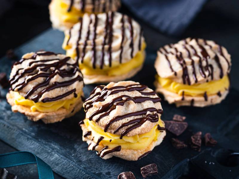 Ferske små kaker med gul krem og sjokoladestriper på toppen, plassert på en svart steinplate.