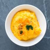 En skål med mos av gulrot og potet, pyntet med litt grønt og pepper.