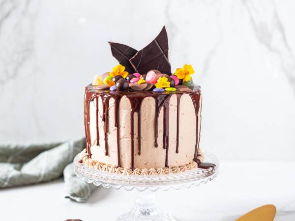 En kake med sjokoladetrekk og dekorasjoner av fargerike små blomster og sjokoladeknapper på toppen.