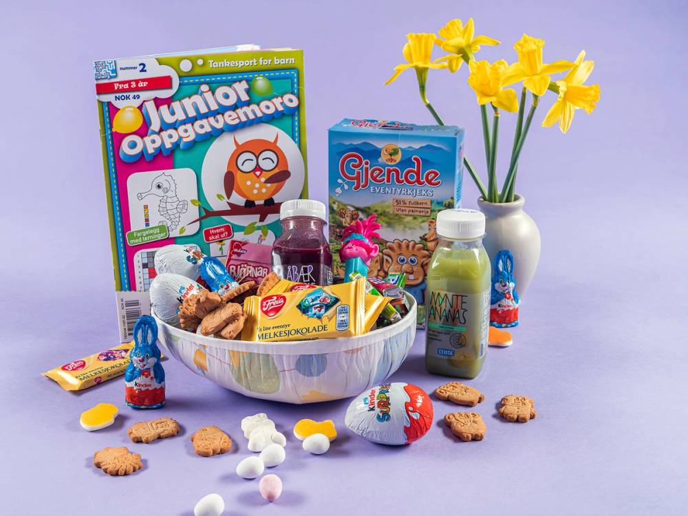 På bildet er det påskeegg, en bok, en vase med gule påskeliljer, en kopp, og ulike godterier og snacks på et bord.