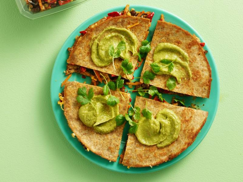 Tortillapizzaer med grønn saus og urter på en blå tallerken, sett på en grønn bakgrunn