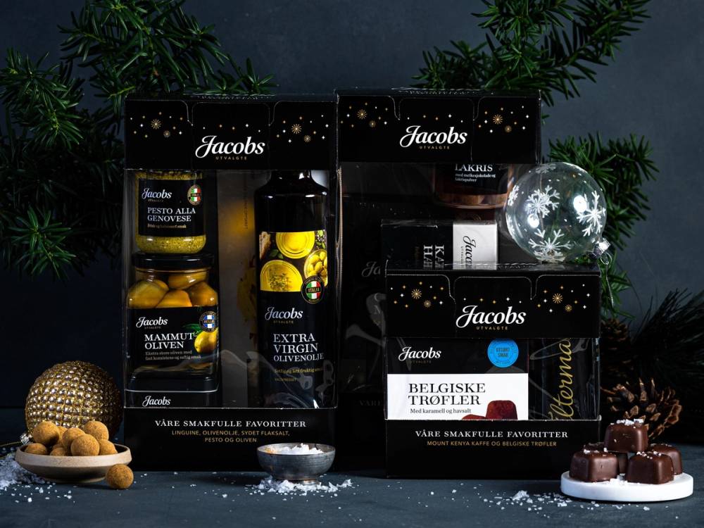 Ulike Jacobs gaveesker og sjokolade på et bord med juledekorasjoner og grønne planter i bakgrunnen.