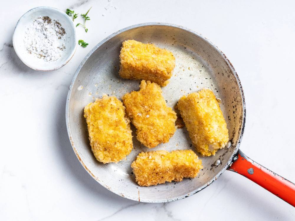 Fiskepinner stekt i en panne med en liten skål med salt ved siden av.