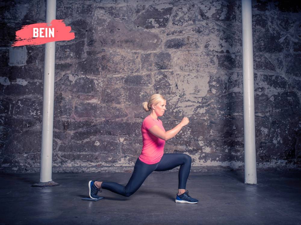 Kvinne i rosa treningtøy gjør utfall foran en murvegg med sklimatte på gulvet.