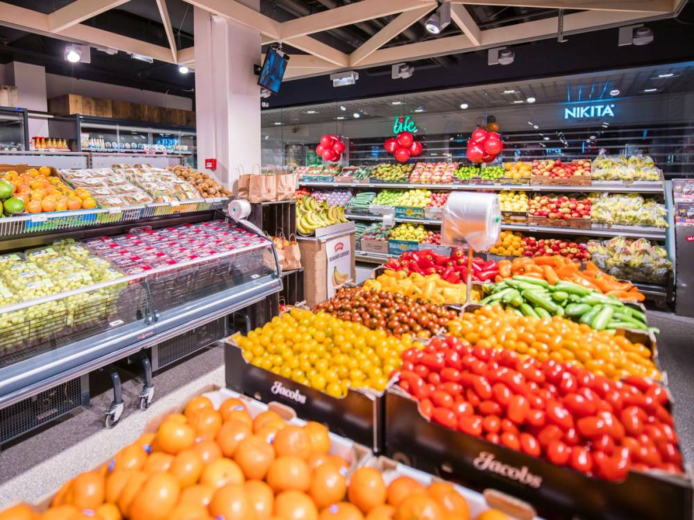 Frukt- og grøntavdeling i en butikk med ulike frukter og grønnsaker på hyller og bord.