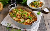 Lapskaus i en stor gryte med grønnsaker og kjøtt, servert med en liten bolle salt og en skje med salt ved siden av.