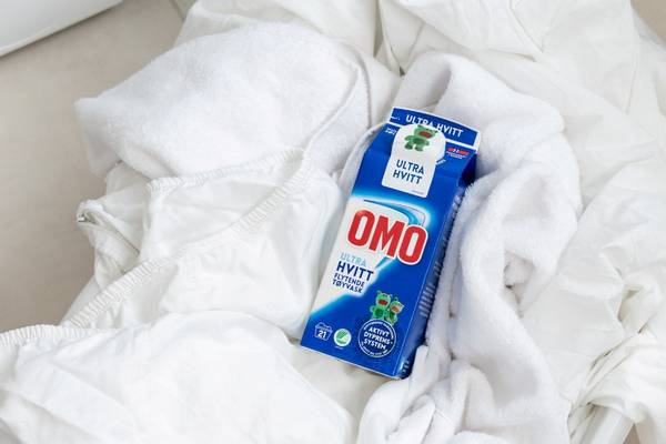 En flaske med Omo Ultra Hvitt vaskemiddel ligger på hvite tekstiler, sannsynligvis klær eller håndklær.