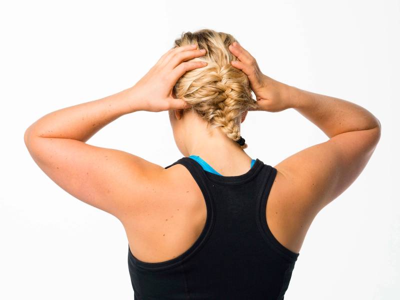 En person med blondt hår som masserer nakken med hendene, sett bakfra.