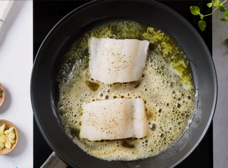 Torskefileter stekes i smør i en panne med litt smør og fett som bobler rundt fisken.
