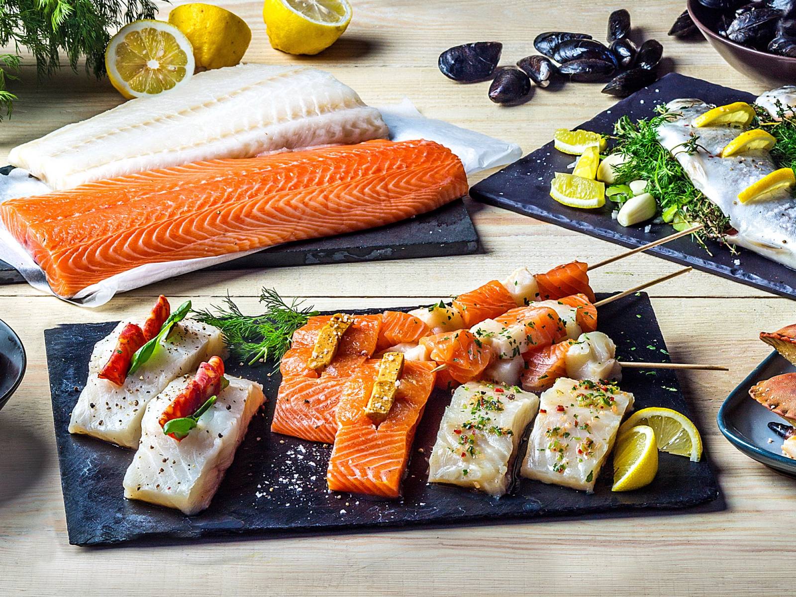 Ulike typer av rå fisk og sjømat, inkludert laks og makrell, presentert på serveringsfat med sitron og urter.