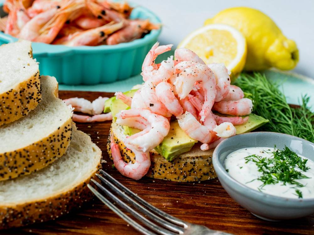 Loff med reker og avokado, servert med sitron og dill, på et fat med grønnsaker i bakgrunnen