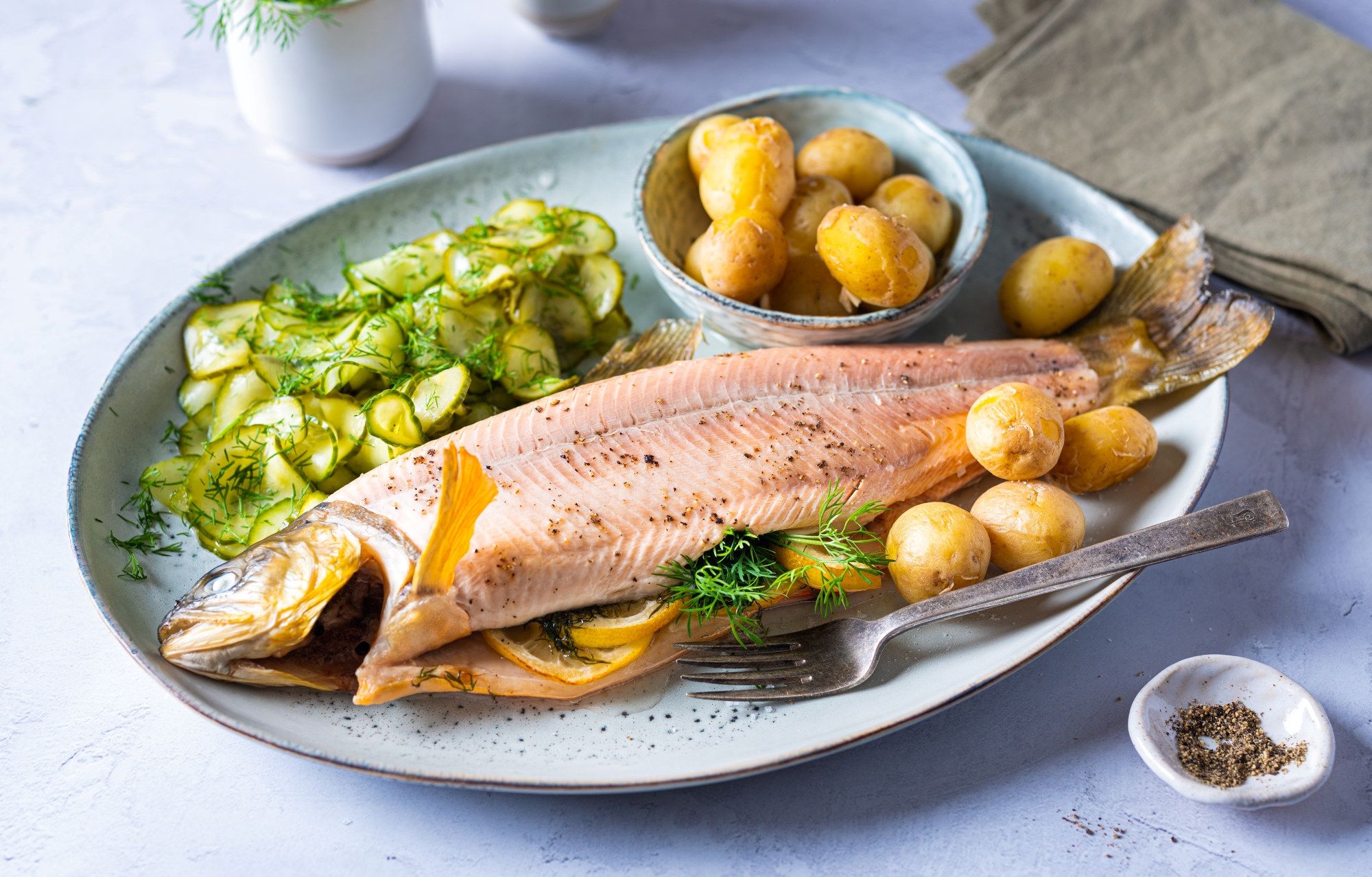 Helstekt telemarksrøye med sitron, poteter og grønnsaker på en oval tallerken.