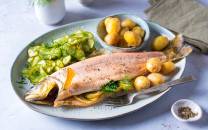 Helstekt telemarksrøye med sitron, poteter og grønnsaker på en oval tallerken.