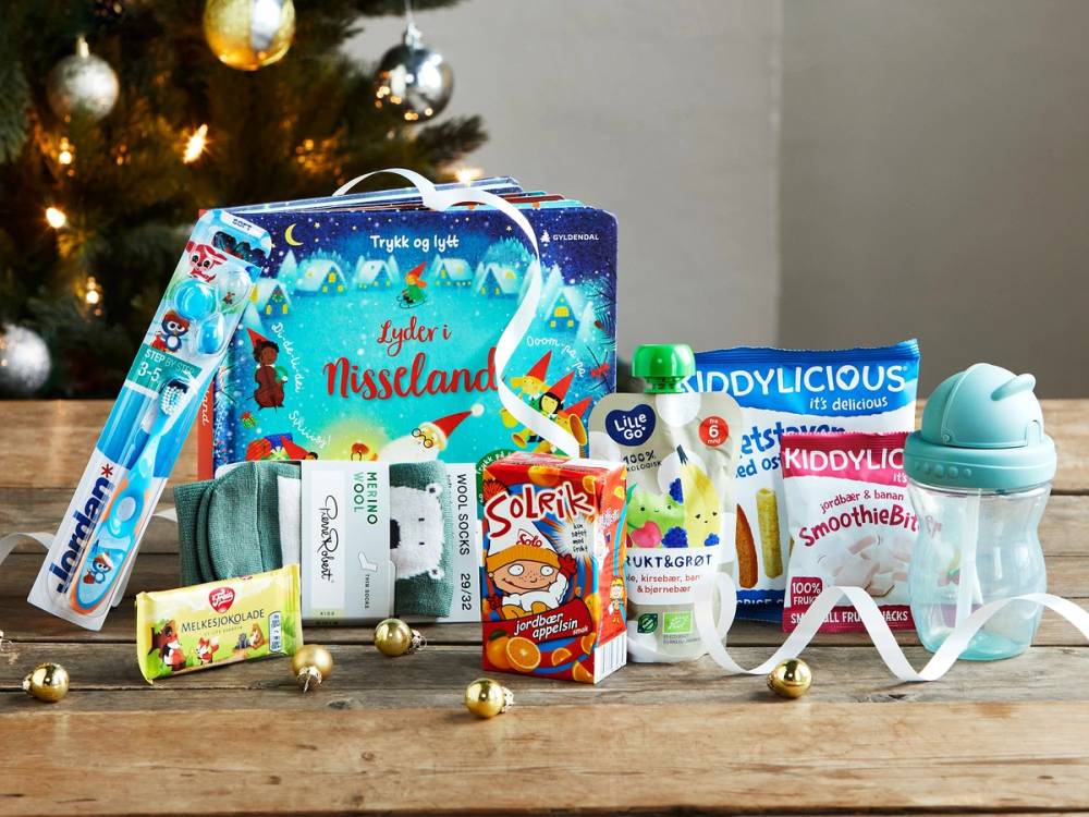 En julekalender med barnevennlig innhold, inkludert tannkrem, tannbørste, leker og godteri, plassert foran en julegran med pynt.