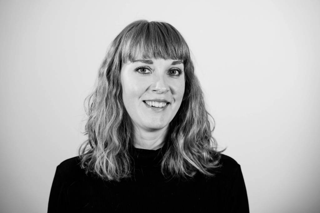 En person med langt, bølget hår som har på seg en svart genser, fotografert mot en lys bakgrunn.