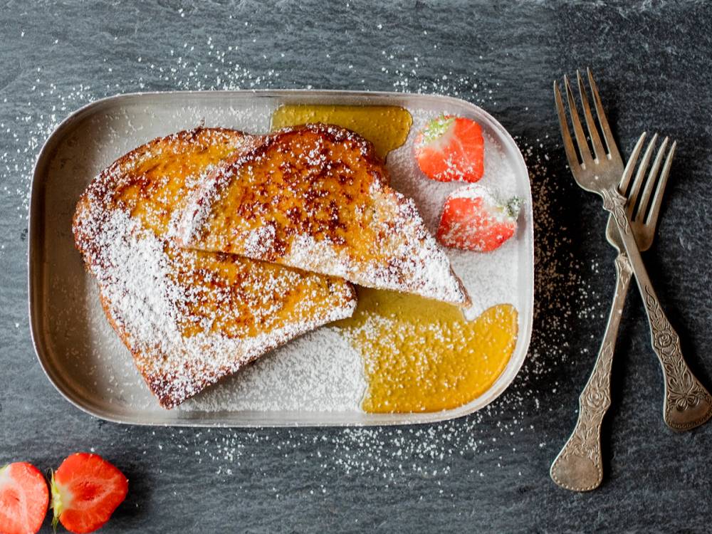 To stykker arme riddere med sukker og sitron på en tallerken, med jordbær og en skje ved siden av.