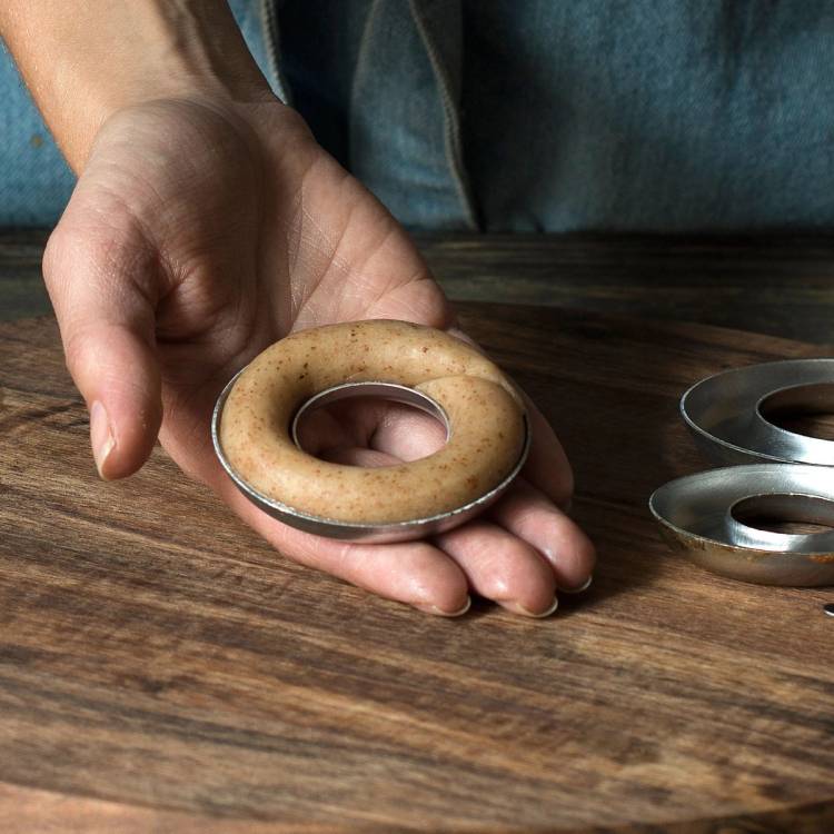 En person holder en rund kransekake i en liten metallform over en treflate, med flere metallformer ved siden av.