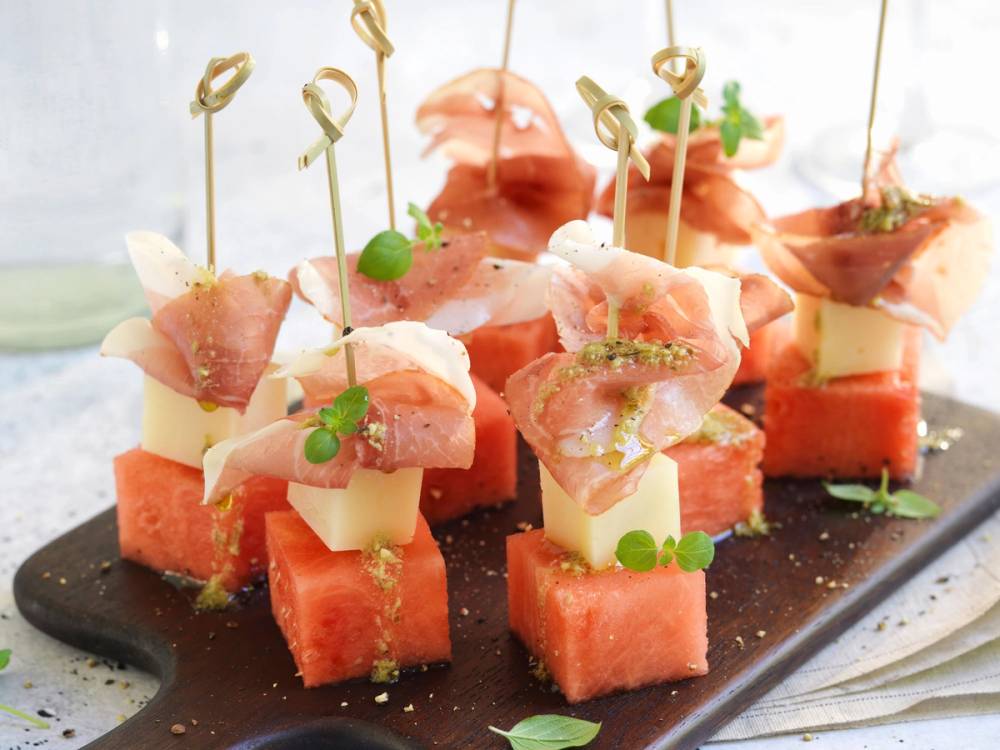 Melonspyd med skinke, manchego-ost og små grønne urter på en svart serveringsplate