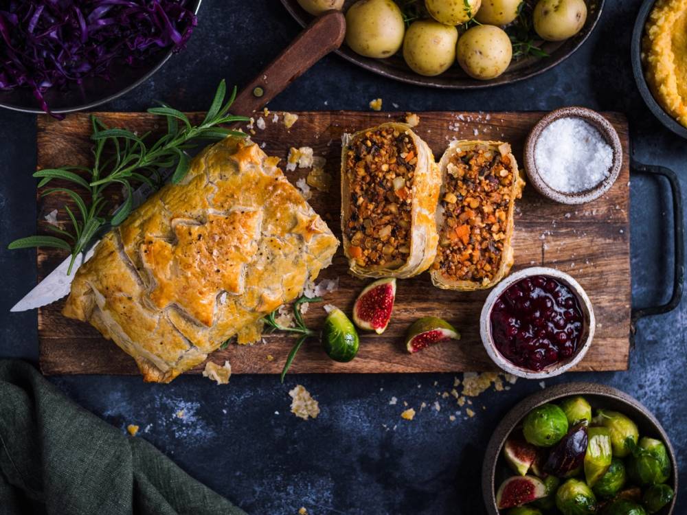 Nøttestek med tilbehør på et skjærebrett, omgitt av bær og krydderurter, klar til servering.