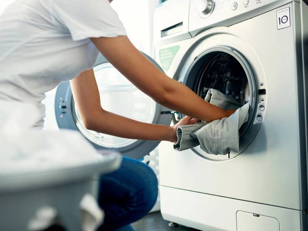 En person legger inn klær i en frontlaster vaskemaskin for å rense den.