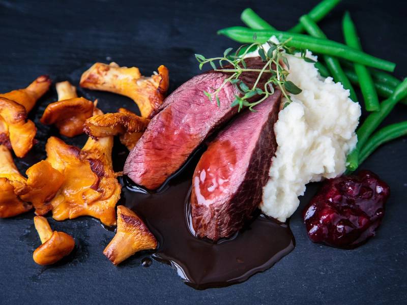 Stekt kjøtt med saus, potetmos, grønne bønner og tyttebær på en svart tallerken