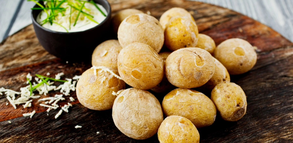 Små, kokte poteter på et skjærebrett med en skål med rømme og frisk dill ved siden av.