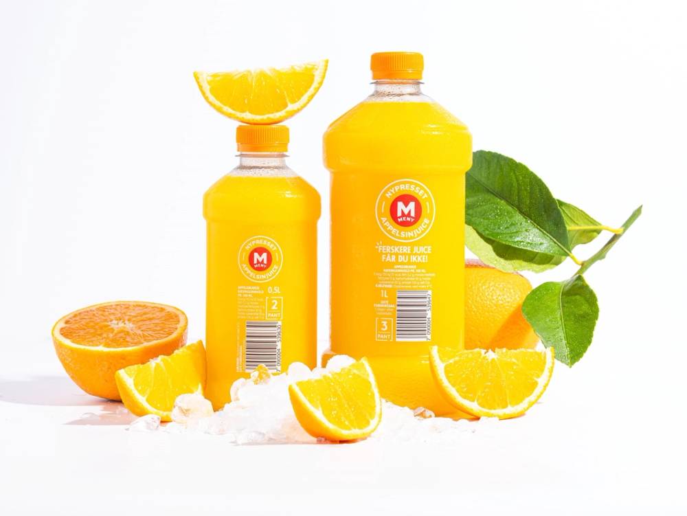 Ferskpresset appelsinjuice i en butikk med hele og skivede appelsiner og grønne blader rundt.