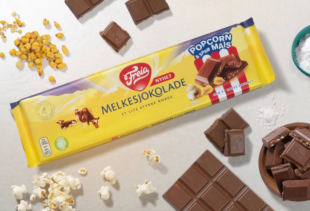 Melkesjokolade med popcorn rundt på en hvit bakgrunn, noen sjokoladestykker og popcornbiter spredt rundt.