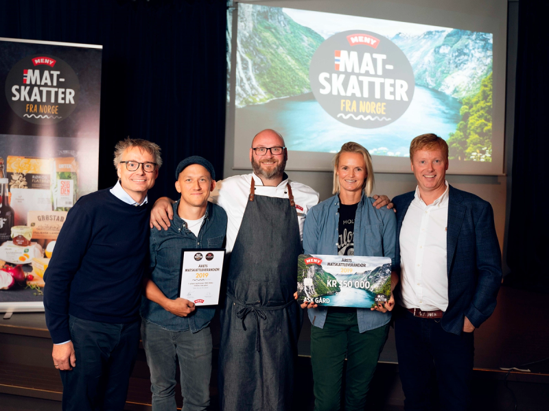 Gruppemedlemmer som mottar matskattstipendet 2019 under en seremoni, med en presentasjonsskjerm i bakgrunnen.