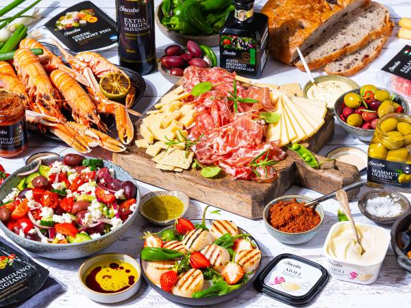 Et utvalg av middelhavsretter med ost, skinke, oliven, tomatsalat, brød og olivenolje på et bord.