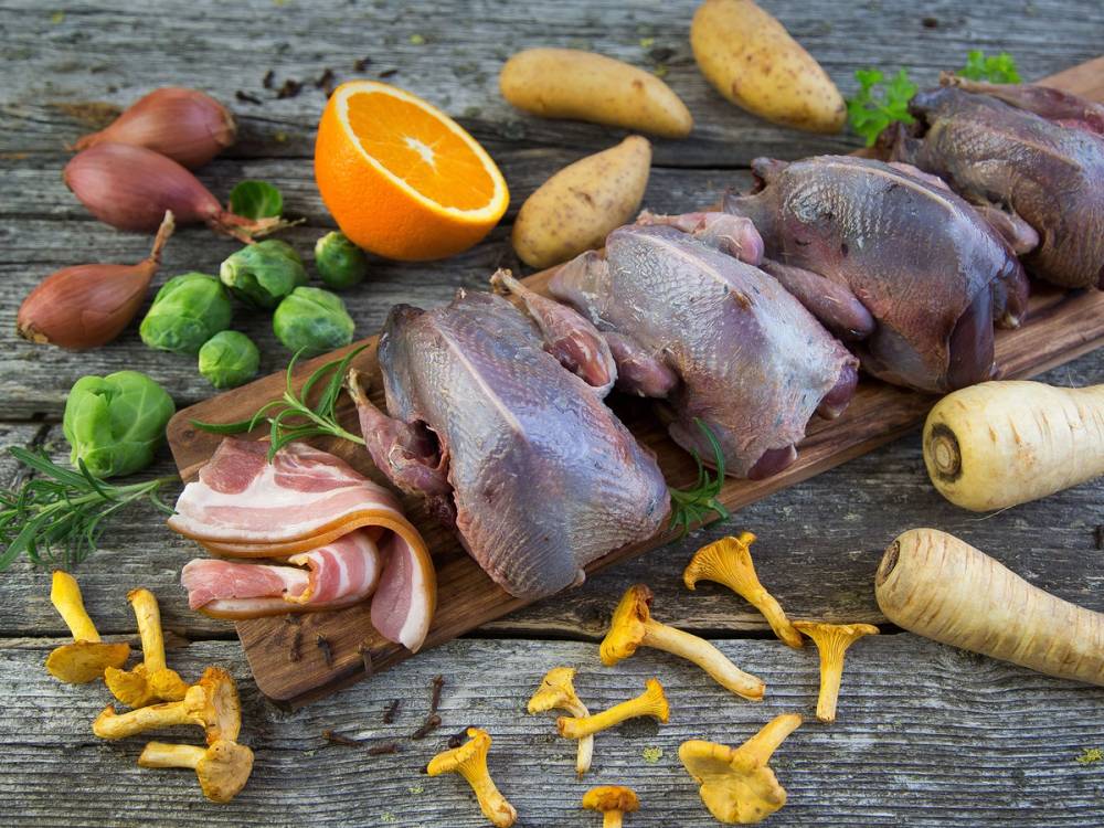 Ulike råvarer som grønnsaker, poteter, og rått kjøtt med sopp på en treplate, klar til matlaging.