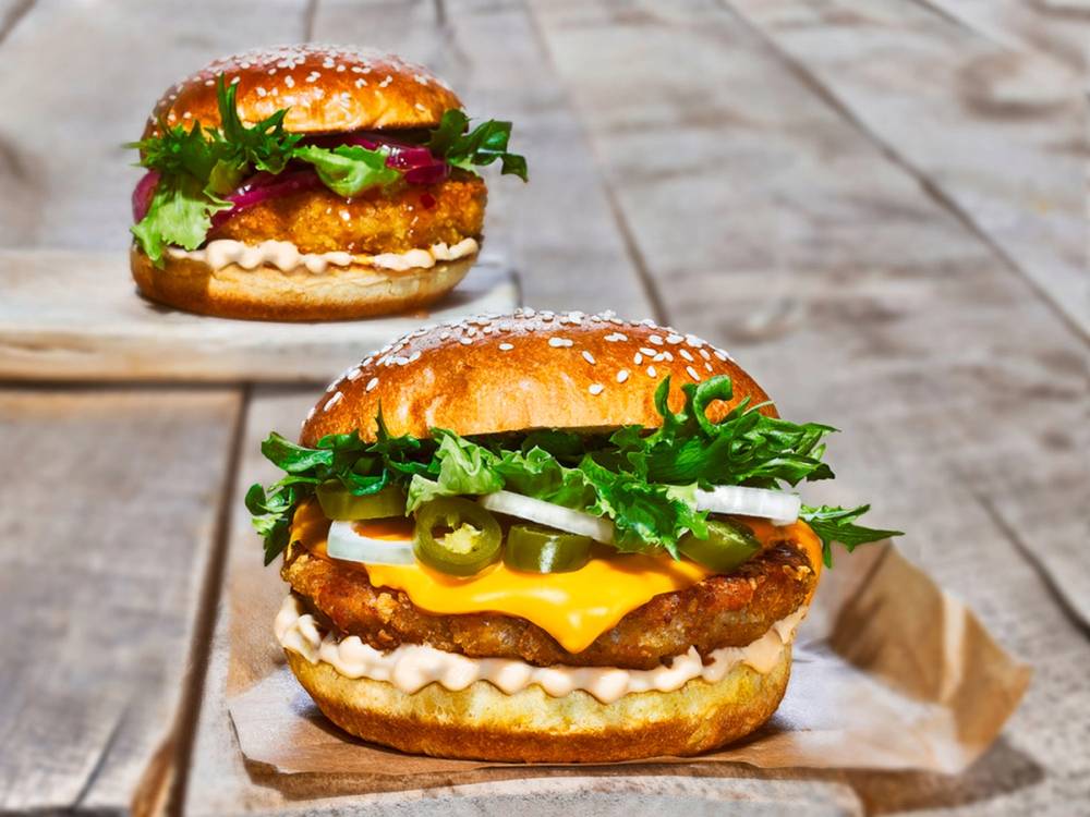 To crispy burgere med ost, salat, pickles og saus på brød, plassert på et tre- eller steinbord.