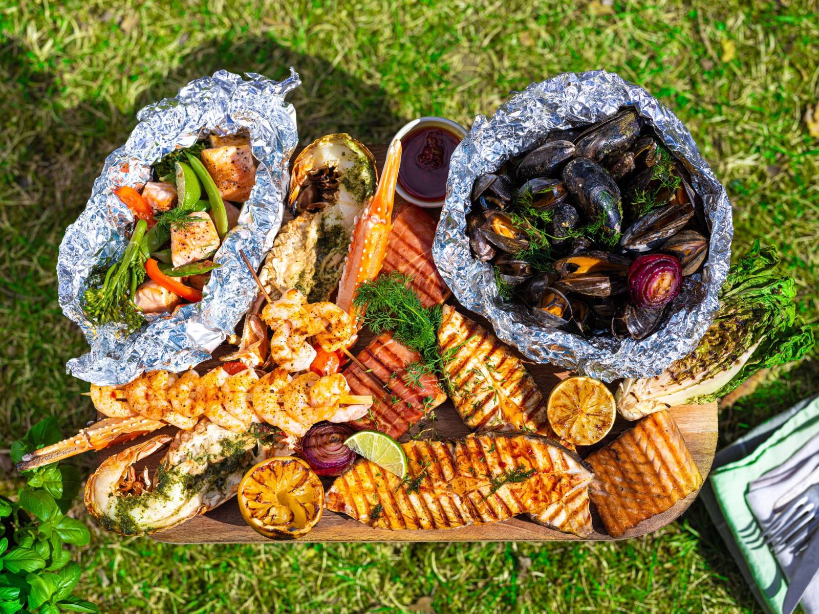 Et utvalg av sjømat, inkludert skalldyr og fisk, servert på et fat med grønnsaker og sitron, med en bakgrunn av gress.