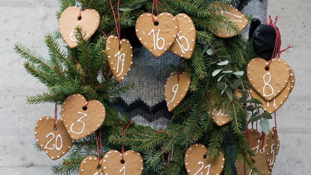 Julegrener med hjerteformede pepperkaker med tall, som er en adventskalender, hengt opp på en vegg.