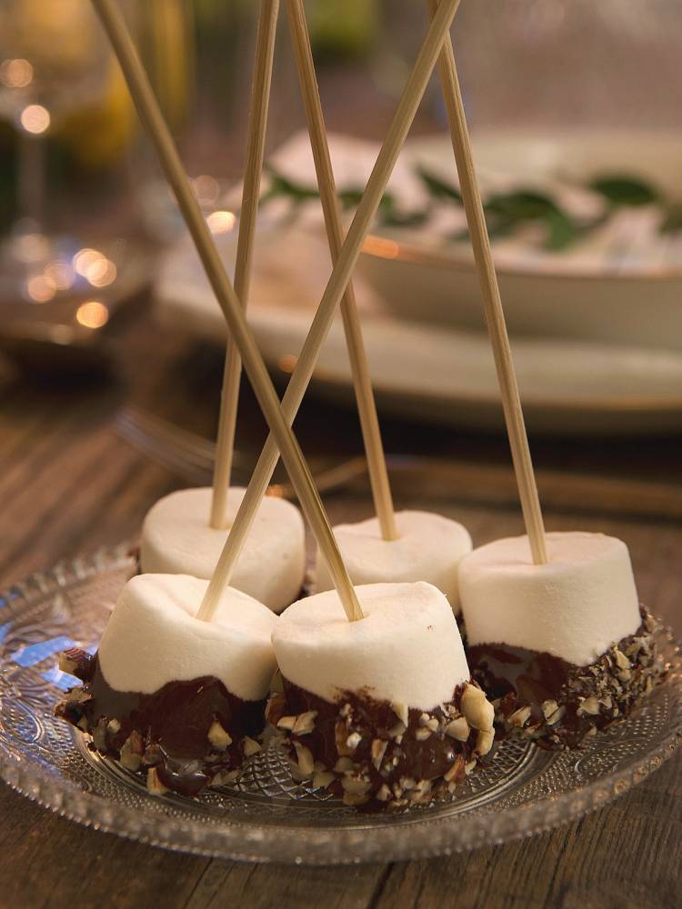 Marshmallows dyppet i sjokolade og strødd med hakkede nøtter på et glassfat.